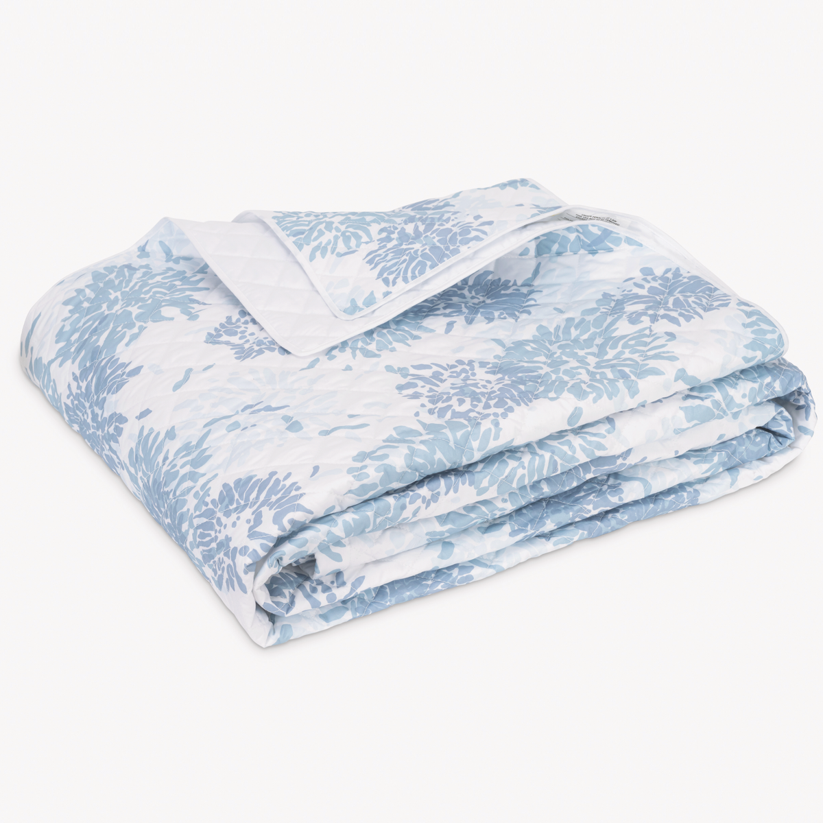 A folded Matouk Chrysanthemum bedding quilt with a blue and white floral pattern