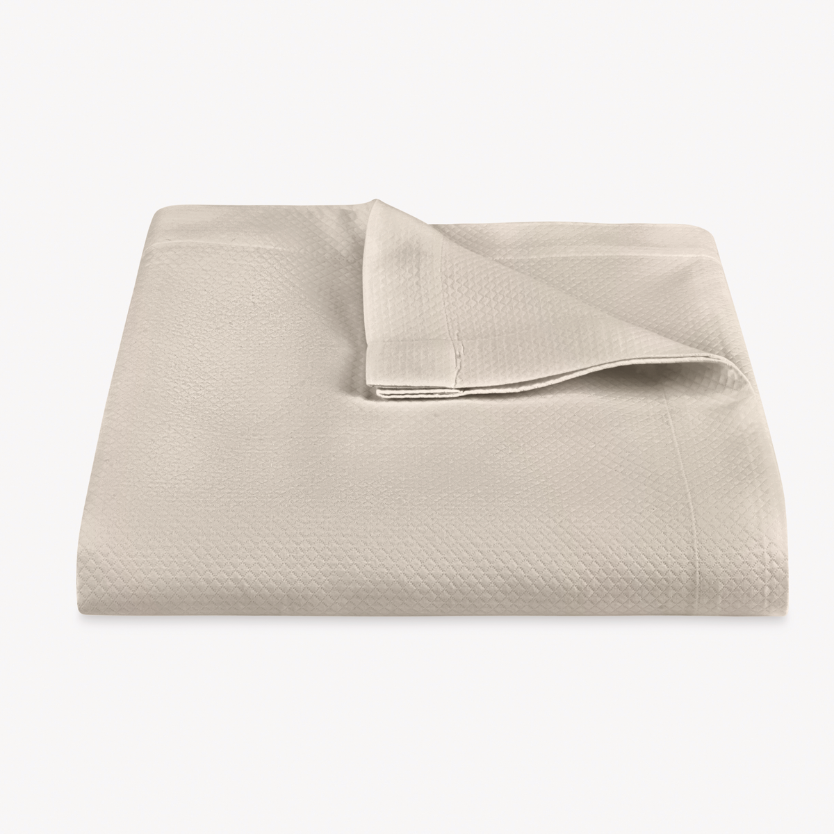 A folded Dune color Matouk Elliot Coverlet with a corner turned down, shown on a plain white background.