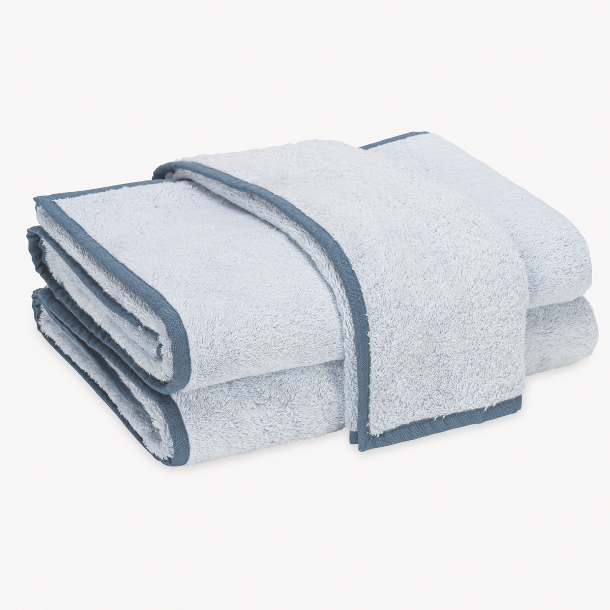 A stack of folded Light Blue and Sea Matouk Enzo Bath Towels on a plain white background.