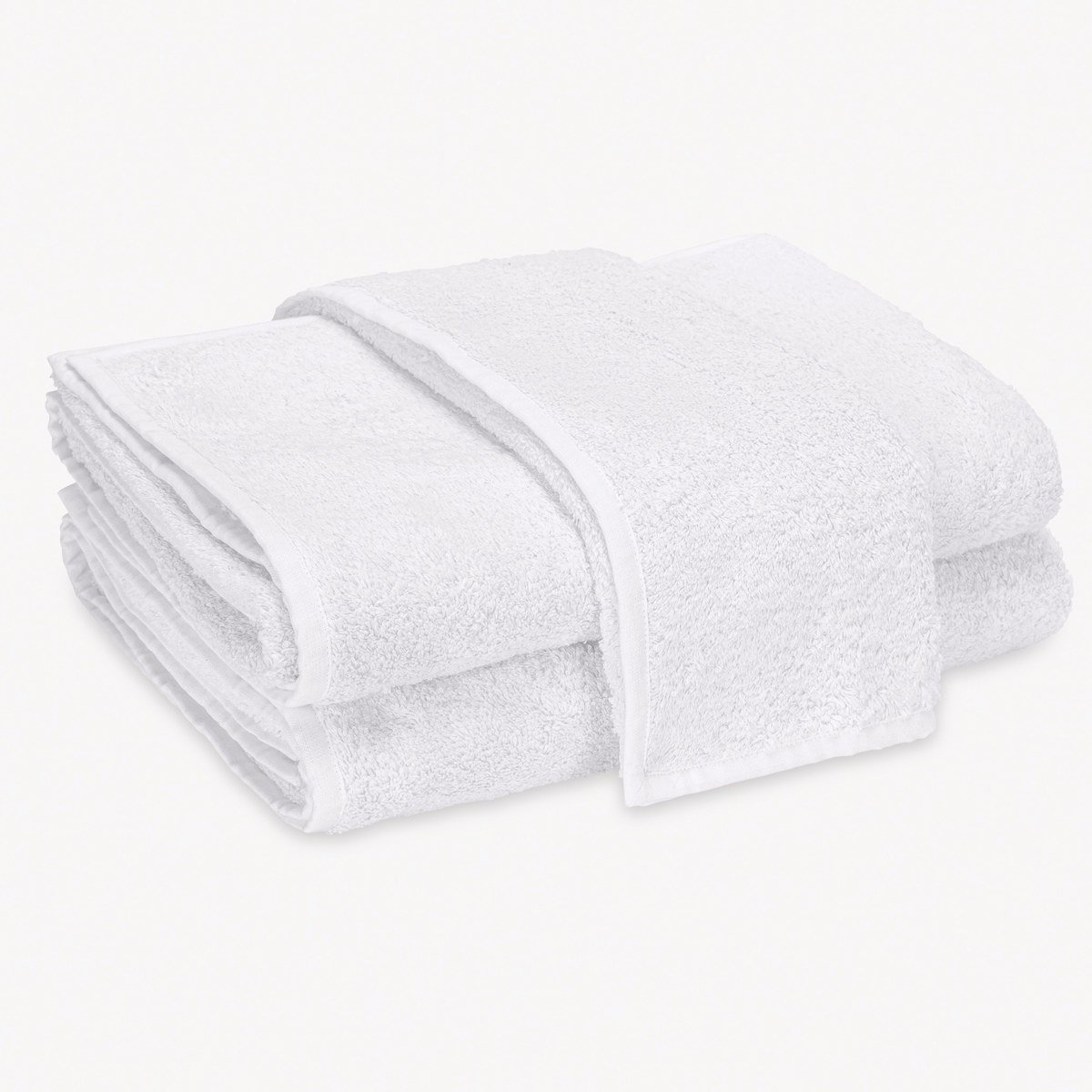 A stack of folded White Matouk Enzo Bath Towels on a plain white background.