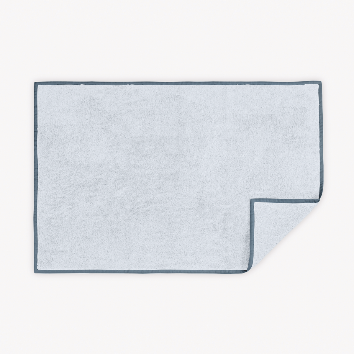 Light Blue Sea Matouk Enzo Tubmat with one corner slightly folded over on a white background