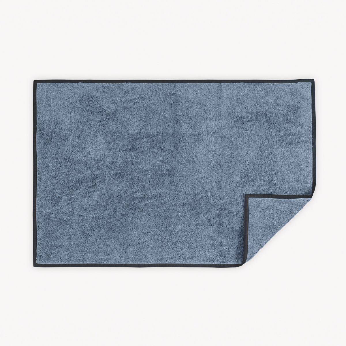 Sea Ink Matouk Enzo Tubmat with one corner slightly folded over on a white background