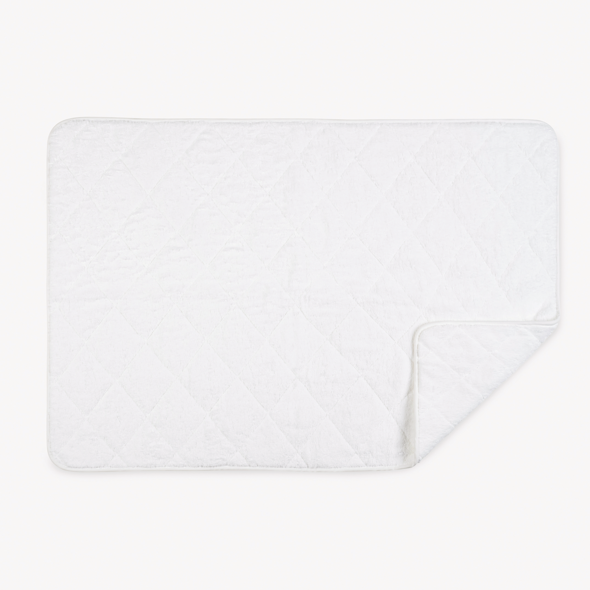 A white quilted rectangular mat with rounded corners, crafted for luxury like Matouk Giza Towels, one corner folded over.
