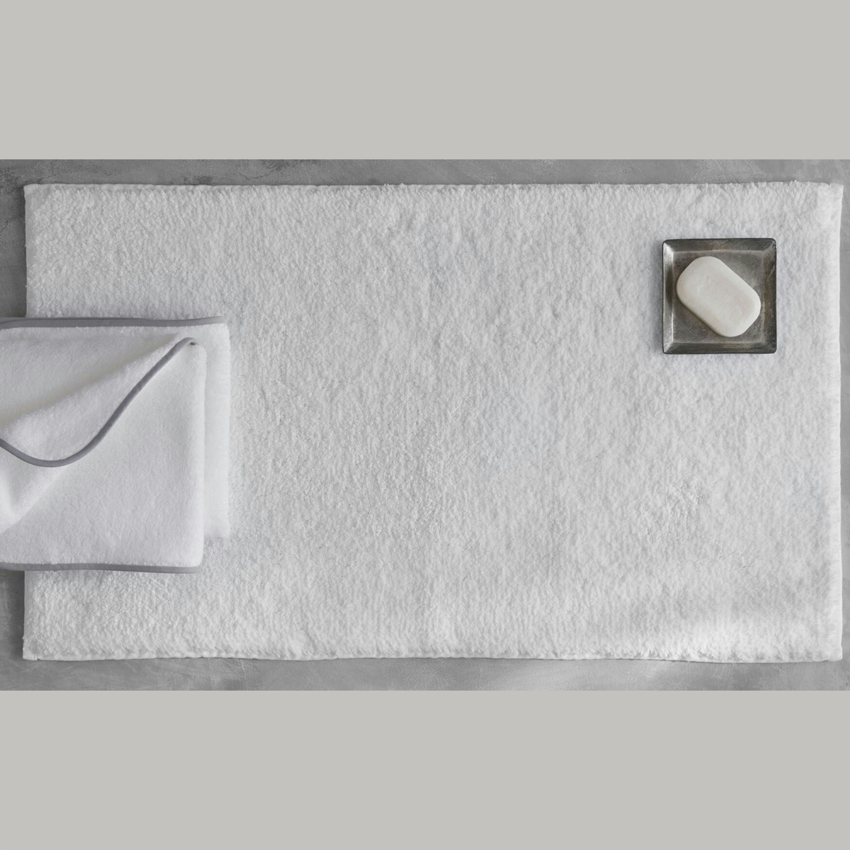 Top view of a White Matouk Giza Bath Rug with a soap and folded towels
