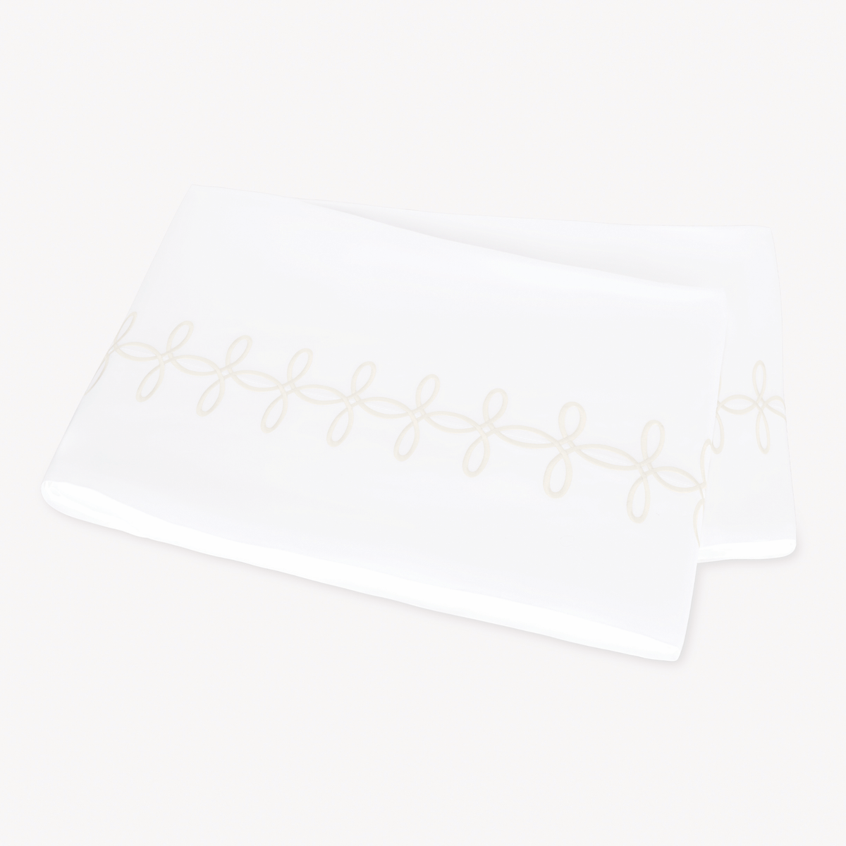 A folded Matouk Gordian Knot Flat Sheet with Cream color embroidery