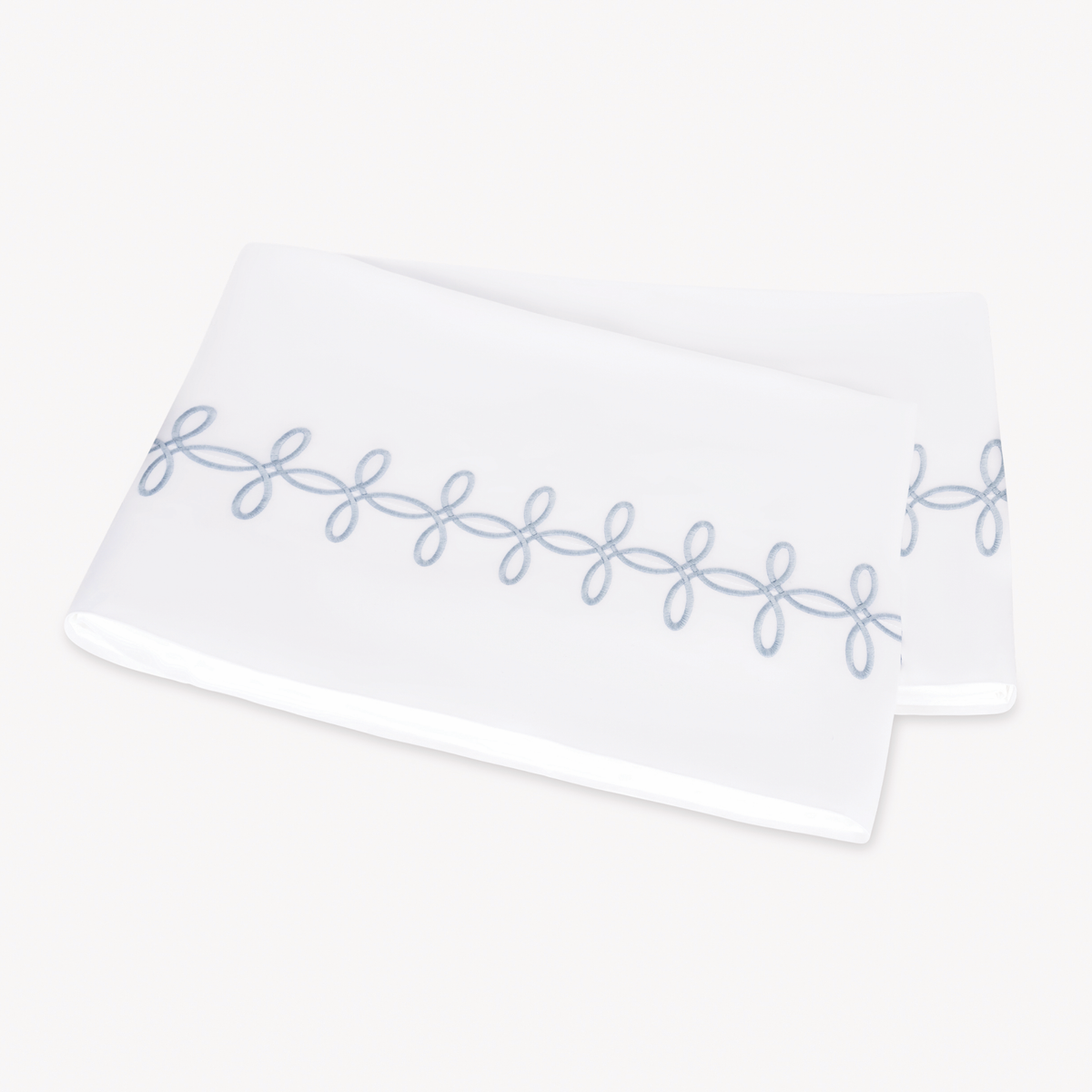 A folded Matouk Gordian Knot Flat Sheet with Wedgwood color embroidery