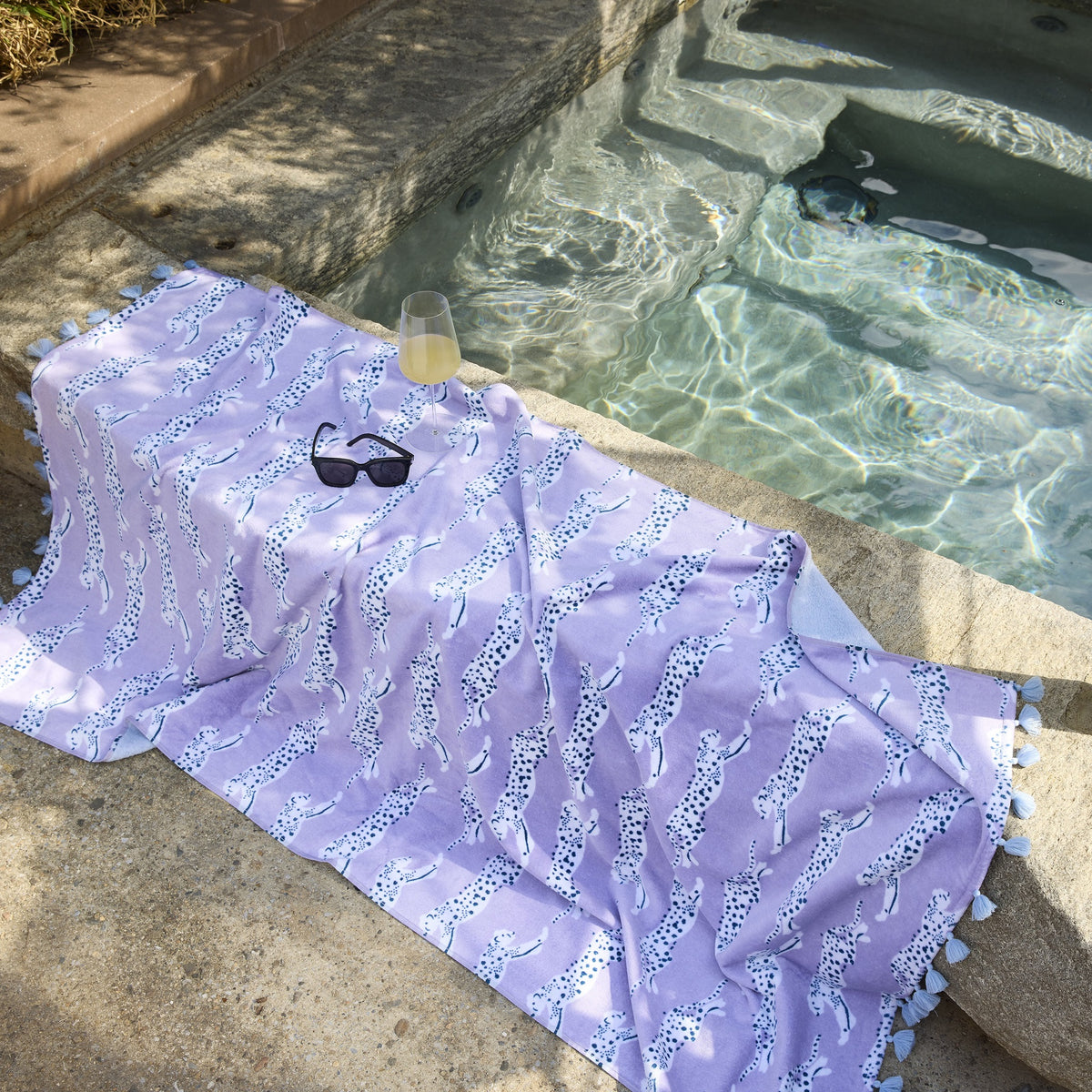 Matouk Leaping Leopard Beach Towels in Color Lilac Layed Out Beside a Pool