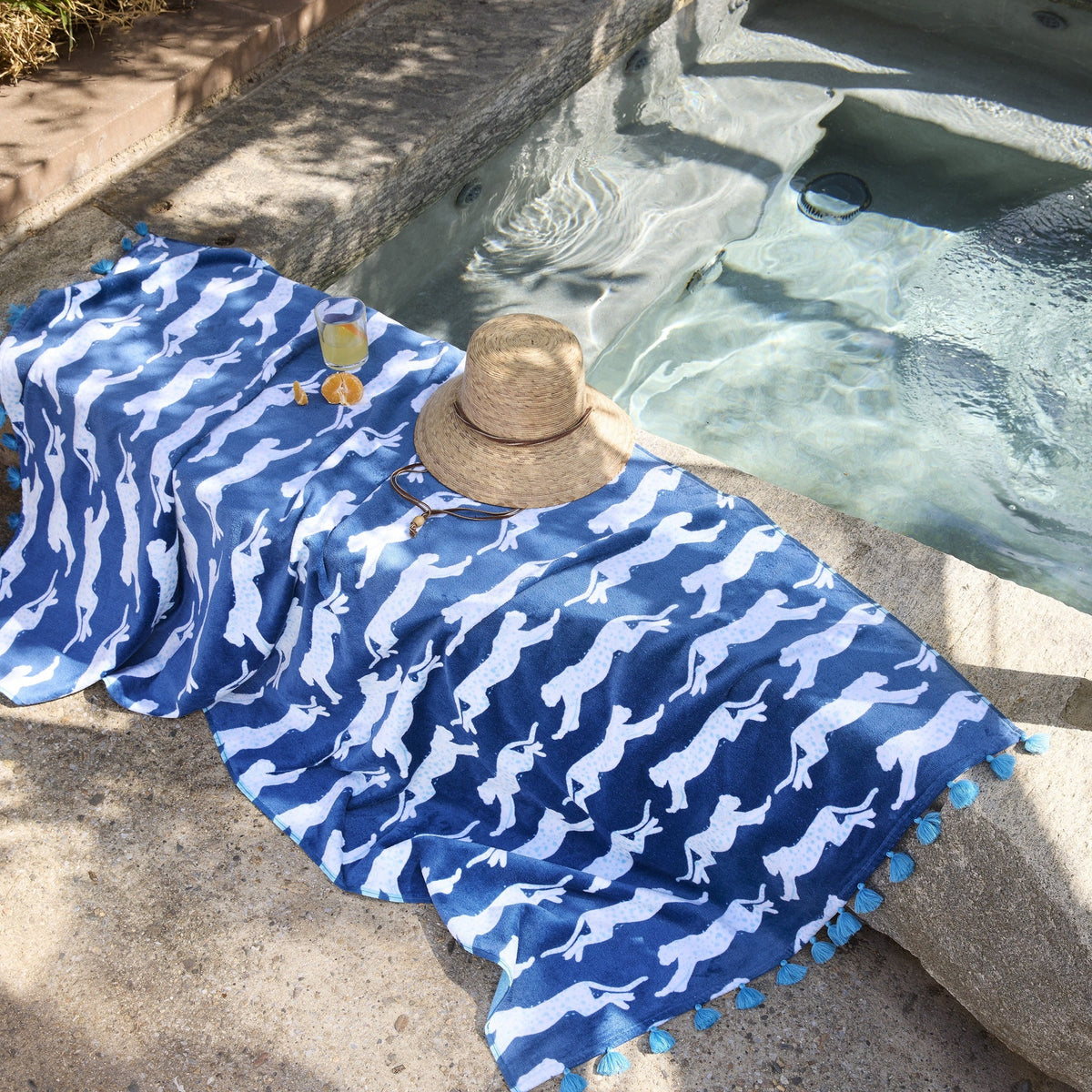 Matouk Leaping Leopard Beach Towels in Color Navy Layed Out Beside a Pool