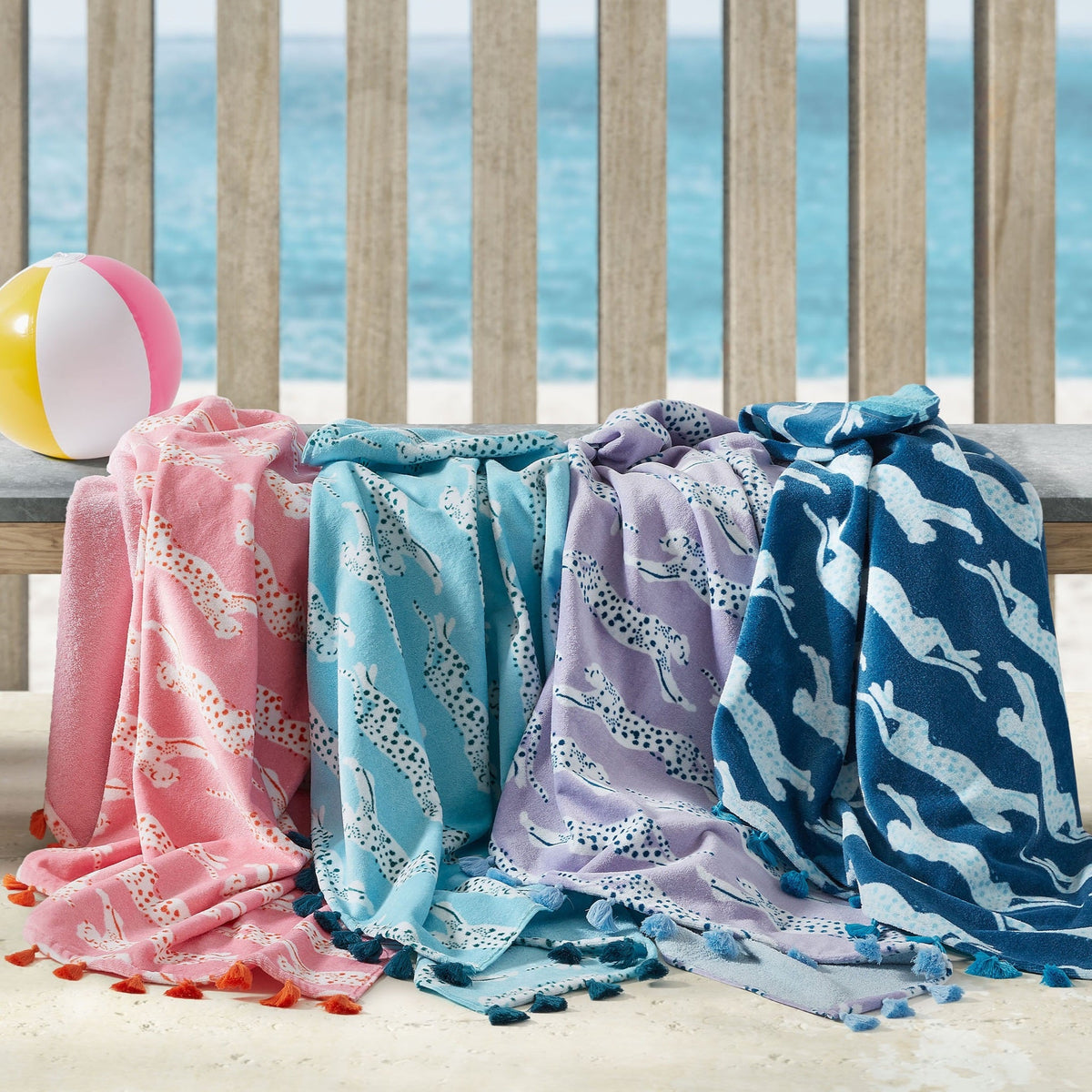 Lifestyle Image of Matouk Leaping Leopard Beach Towels on a Bench in Different Colors