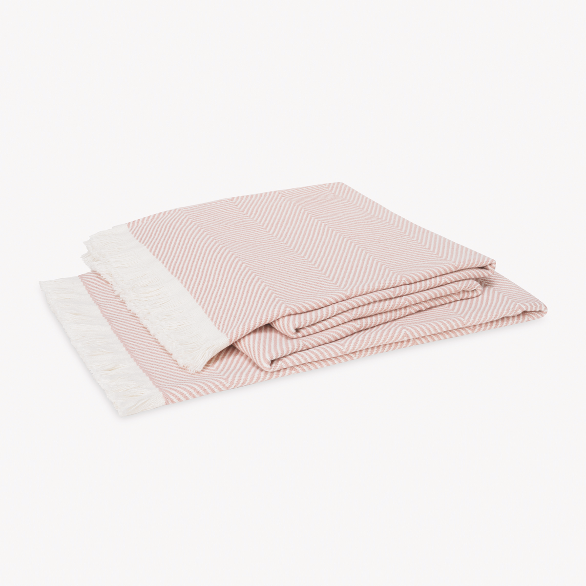 A folded Blush Matouk Leo Throw, a 100% cotton herringbone throw with fringed edges, rests on a plain white background