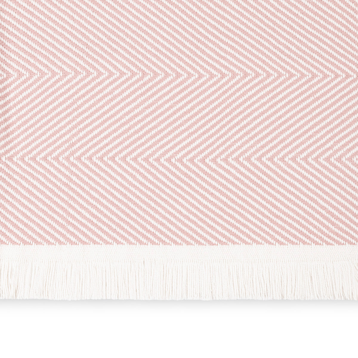 A close-up of a Blush Matouk Leo Throw, a 100% cotton herringbone throw with fringe along the bottom edge