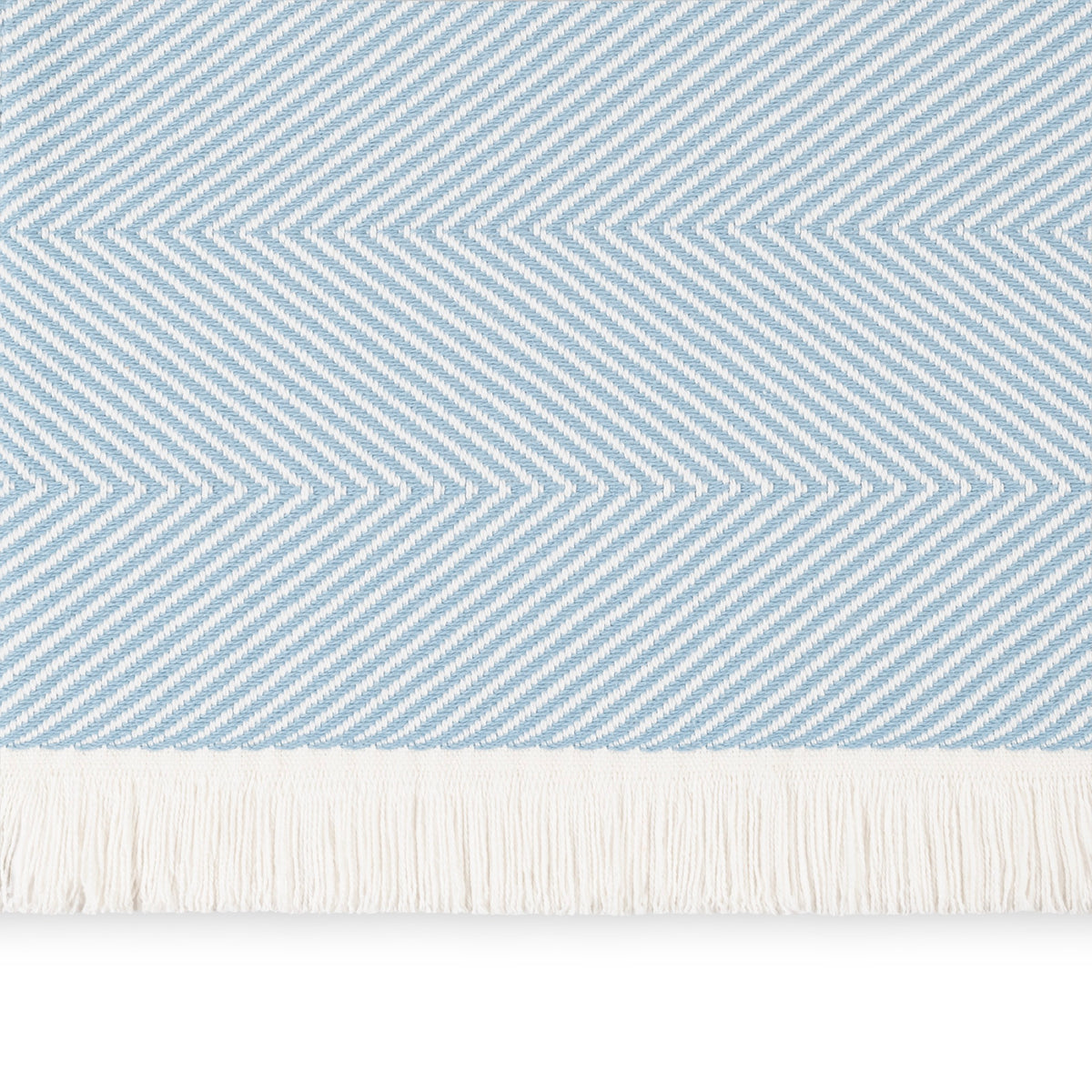 A close-up of a Hydrangea Matouk Leo Throw, a 100% cotton herringbone throw with fringe along the bottom edge