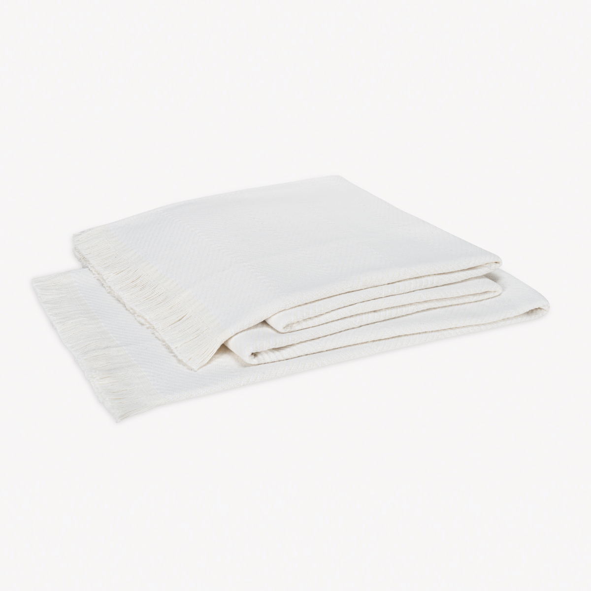 A folded White Matouk Leo Throw, a 100% cotton herringbone throw with fringed edges, rests on a plain white background