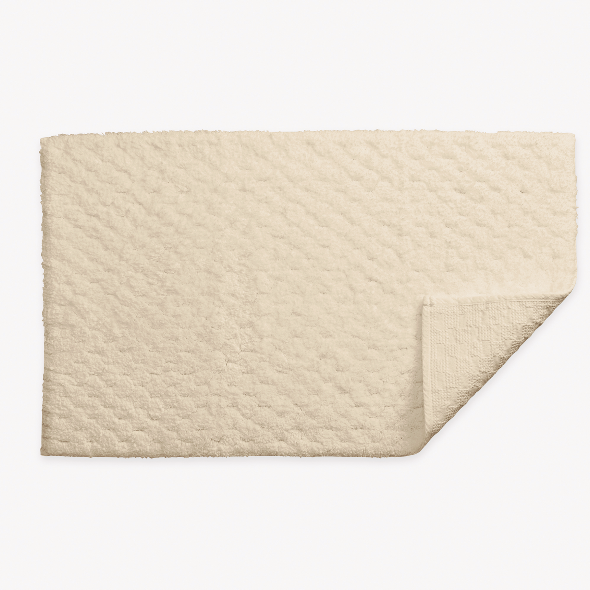A dune rectangular 700 GSM Matouk Lotus Bath Rug  and one corner folded over, shown on a white background