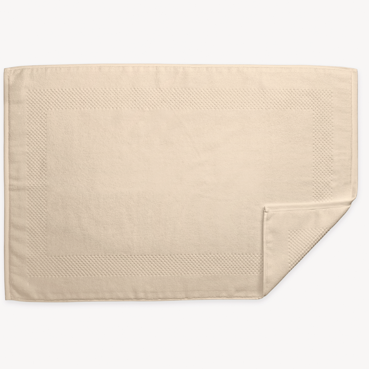 A Dune rectangular 700 GSM Matouk Lotus Tubmat  and one corner folded over, shown on a white background