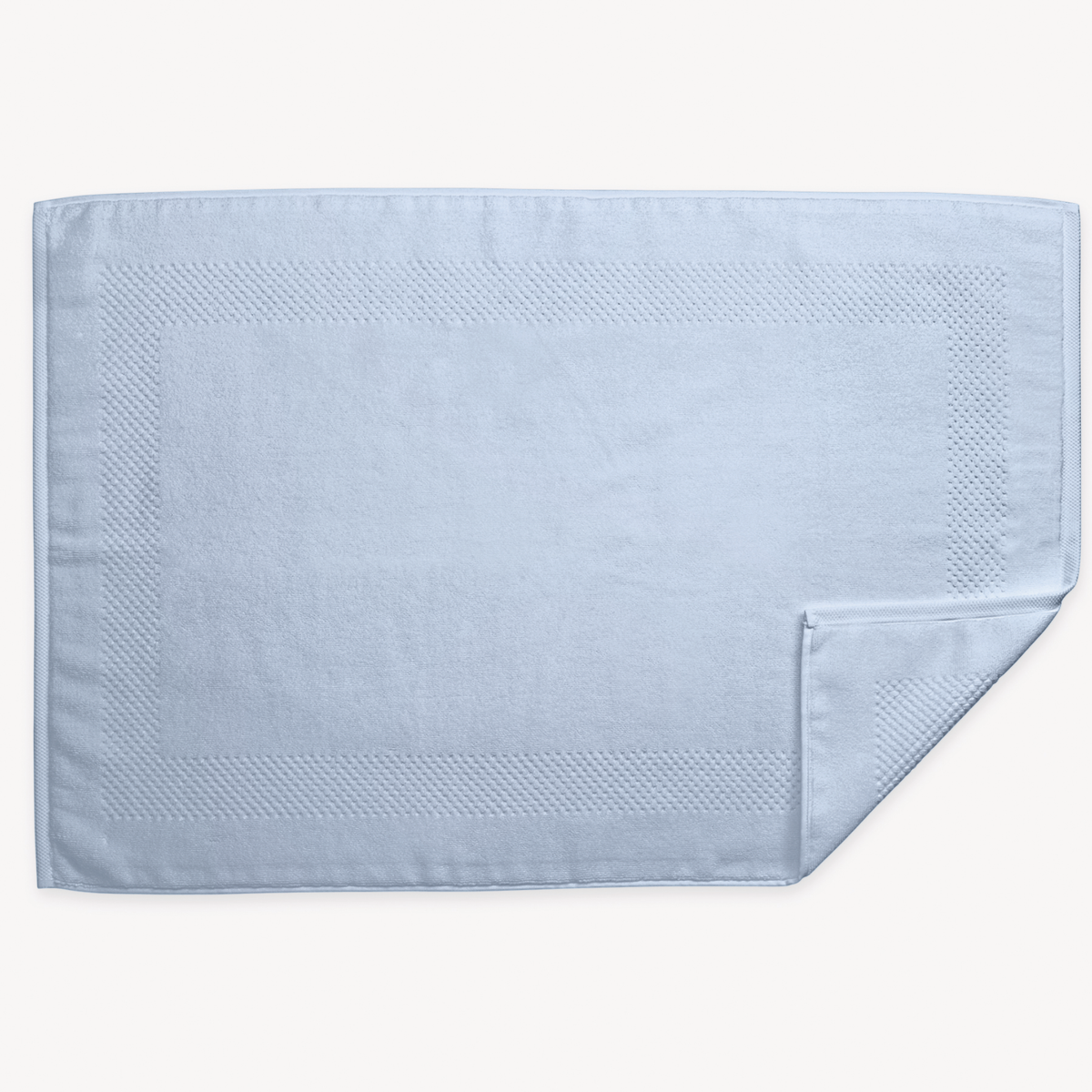 A light blue rectangular 700 GSM Matouk Lotus Tubmat  and one corner folded over, shown on a white background