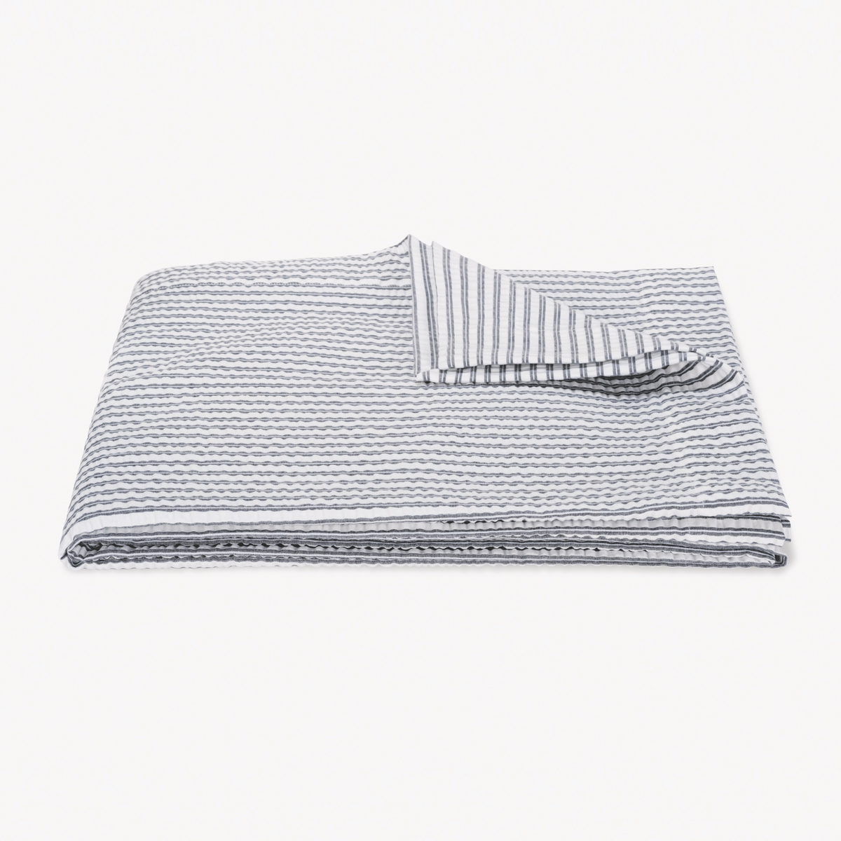 A folded, textured Deepnavy striped coverlet from the cotton seersucker bedding Matouk Matteo Collection