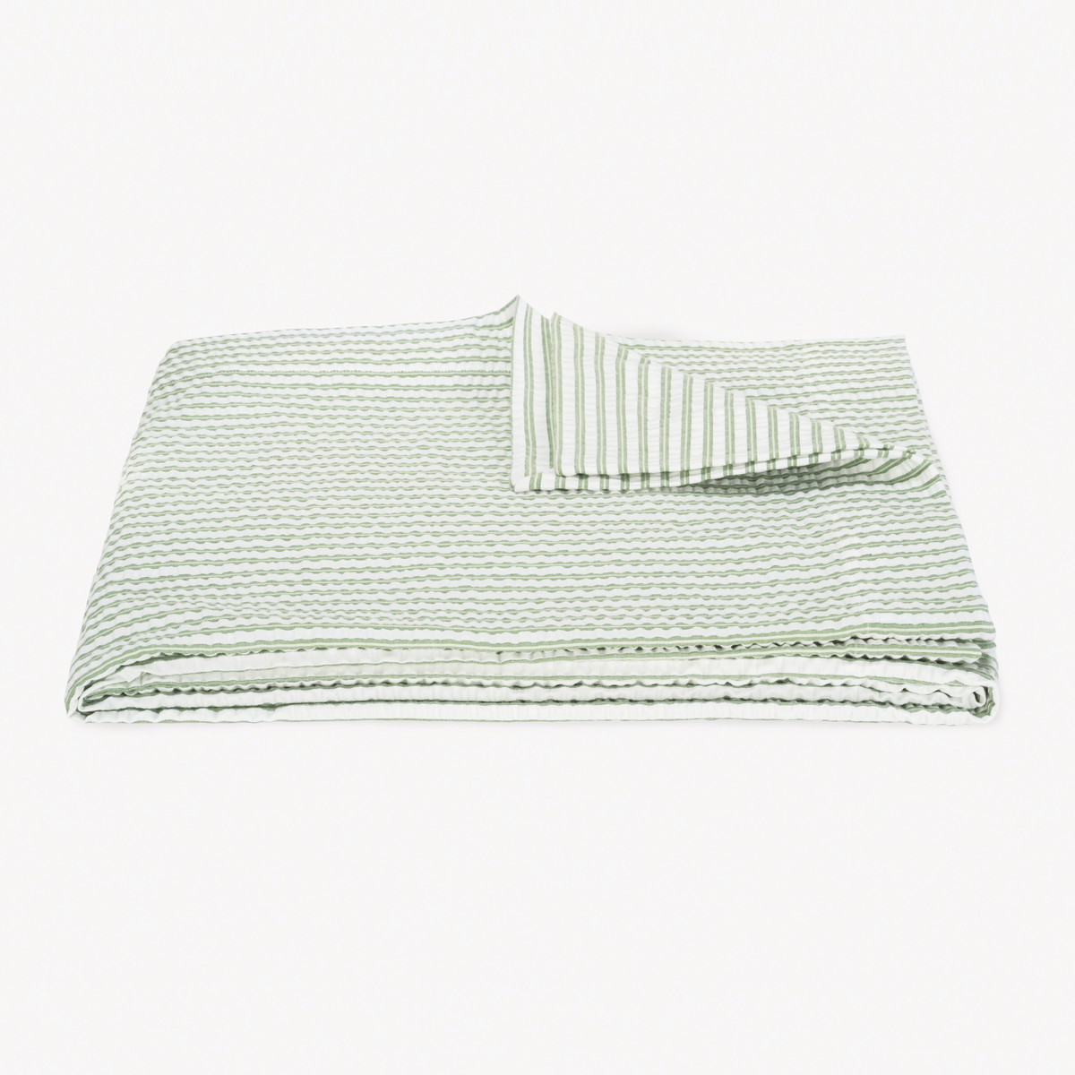 A folded, textured Palm striped coverlet from the cotton seersucker bedding Matouk Matteo Collection
