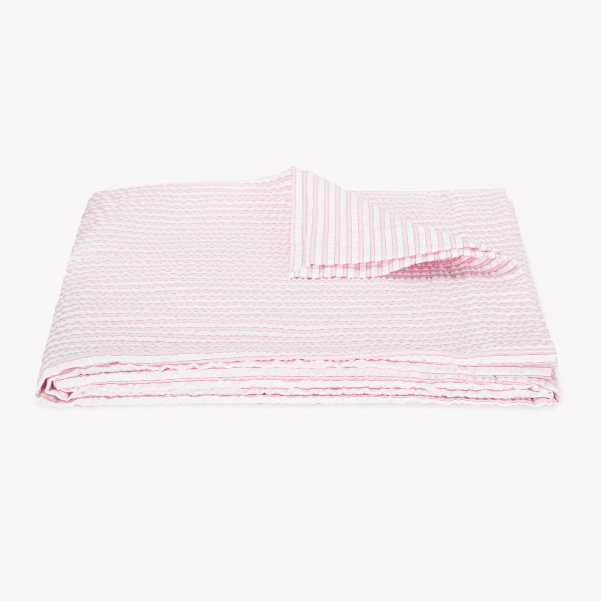 A folded, textured Pink striped coverlet from the cotton seersucker bedding Matouk Matteo Collection