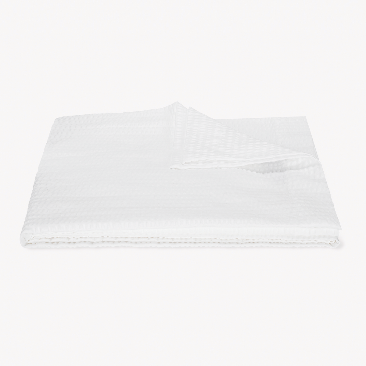 A folded, textured White striped coverlet from the cotton seersucker bedding Matouk Matteo Collection