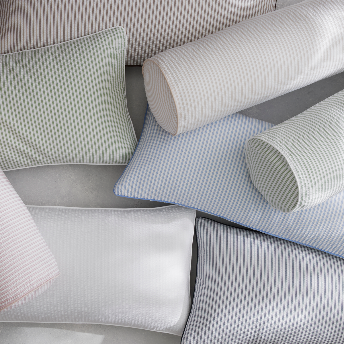 Assorted striped pillows from the Matouk Matteo Collection evoke a menswear-inspired bedroom on a light gray surface.