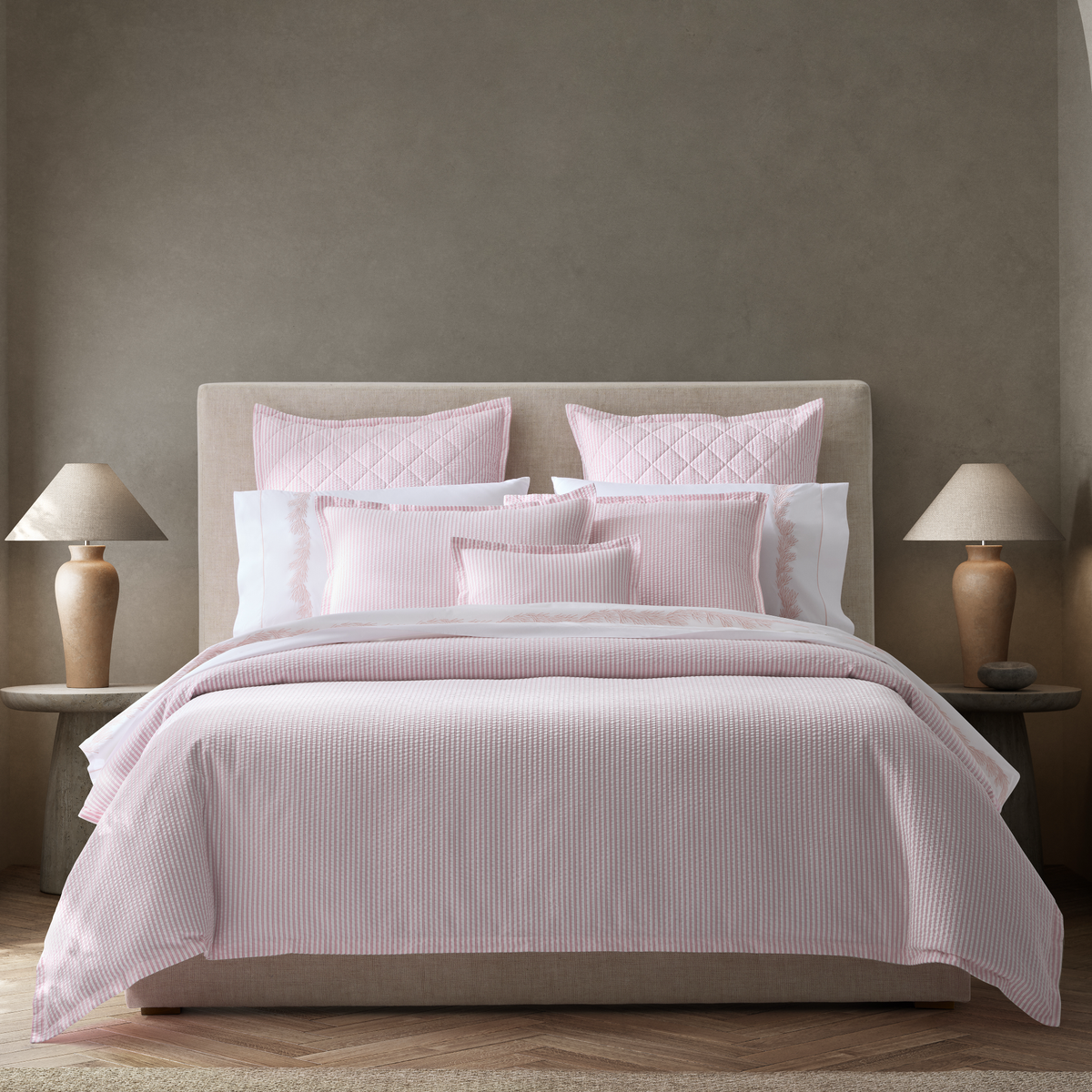 A neatly made bed with Pink Matouk Matteo seersucker bedding, flanked by two wooden nightstands and matching lamps