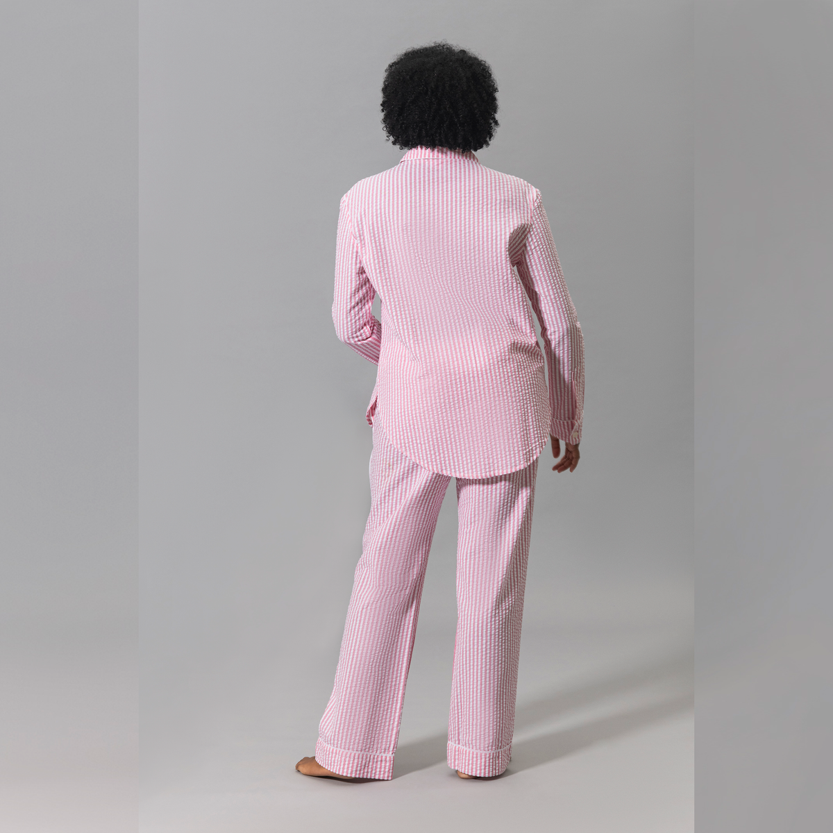 A person stands facing away wearing a pink Matouk Matteo Pajama set against a plain gray background