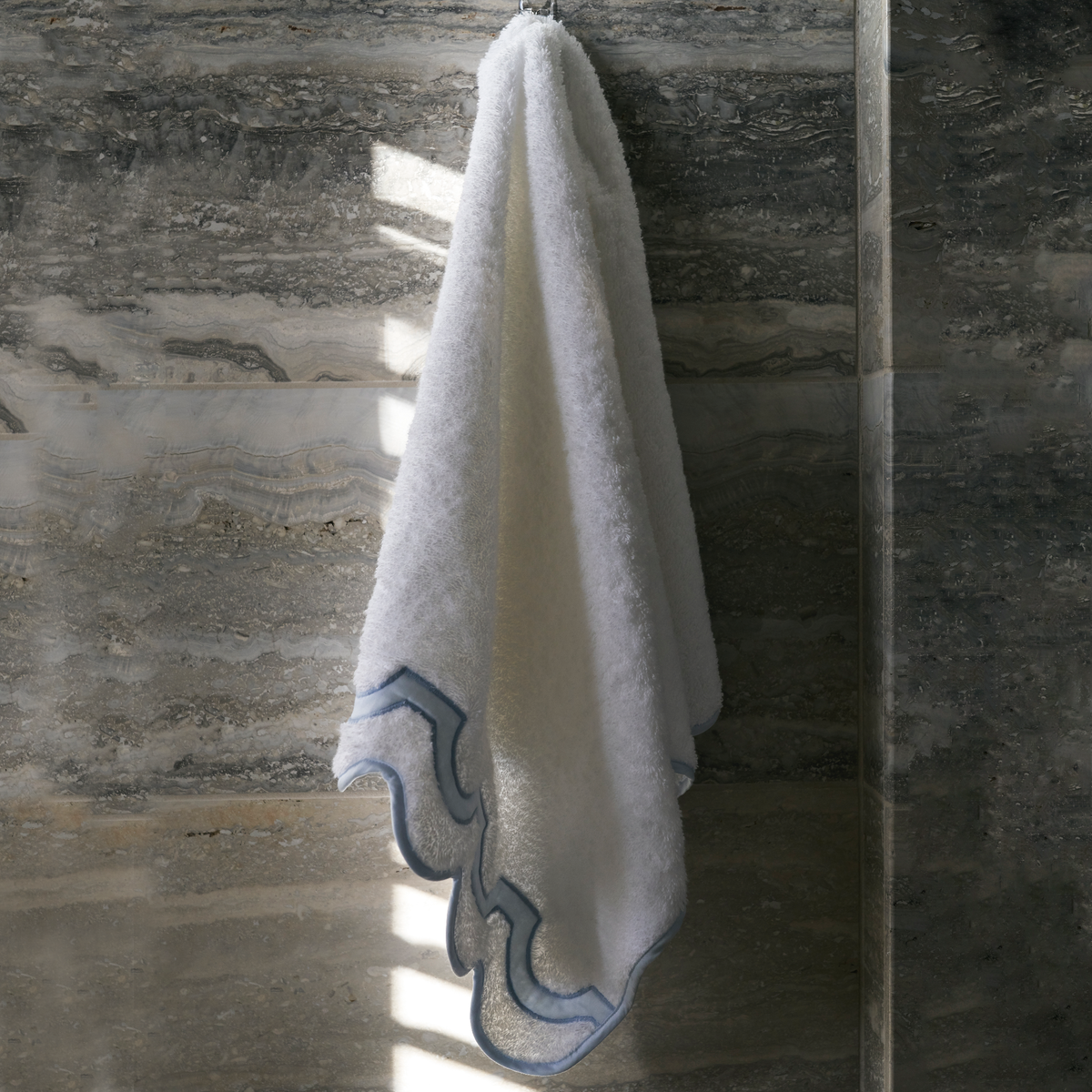 A Matouk Mirasol Bath Towel Hanging by a Bathroom Wall