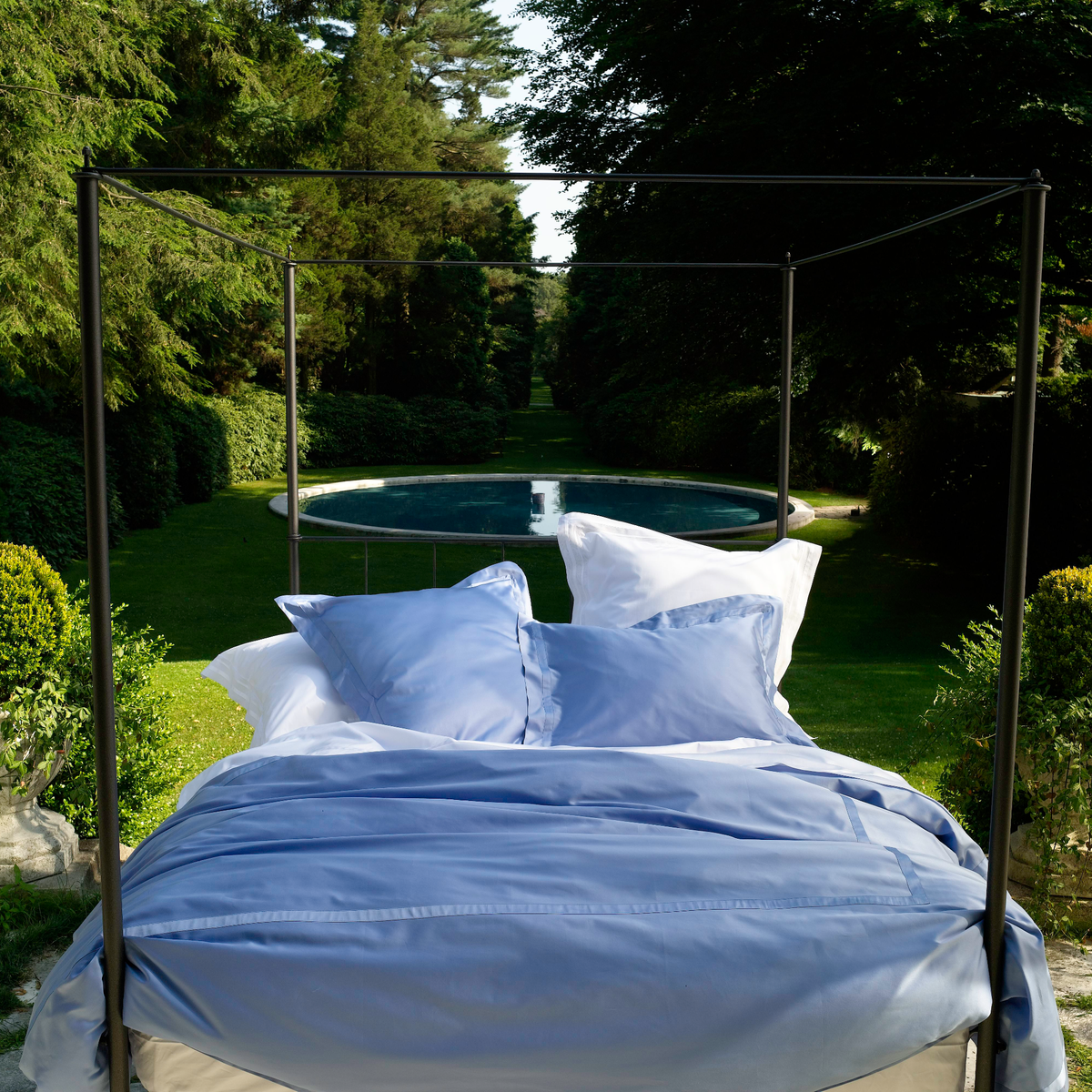 Lifestyle Shot of a Bed Outdoors Dressed in Matouk Nocturne Bedding in Azure Color