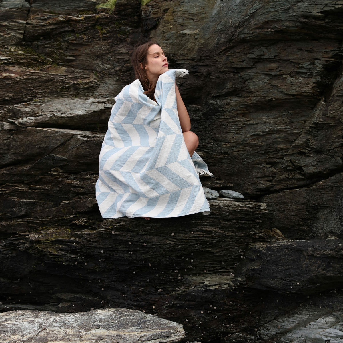 Model Sitting on a Rock with Matouk Paros Beach Towels in Color Ocean
