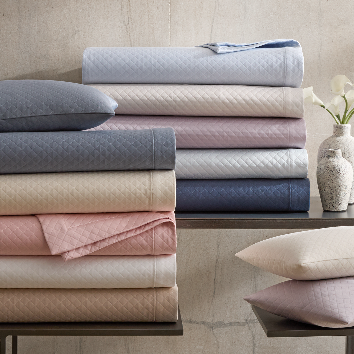 Stacks of folded matelassé coverlets and pillowcases in various colors from Matouk Petra Bedding collection