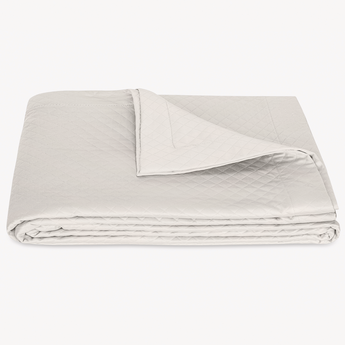 A neatly folded Silver matelassé coverlet blanket from Matouk Petra Bedding with a corner turned back