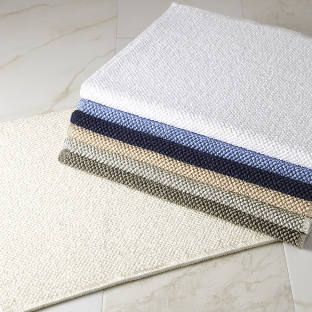 Stack of Matouk Reverie Bath Rugs on the Floor