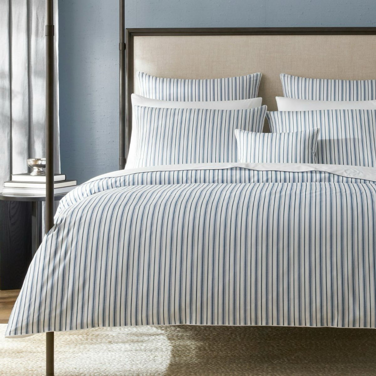 A bed with Matouk Schumacher Calypso Bedding in Prussian Blue collection and a beige headboard against a blue wall