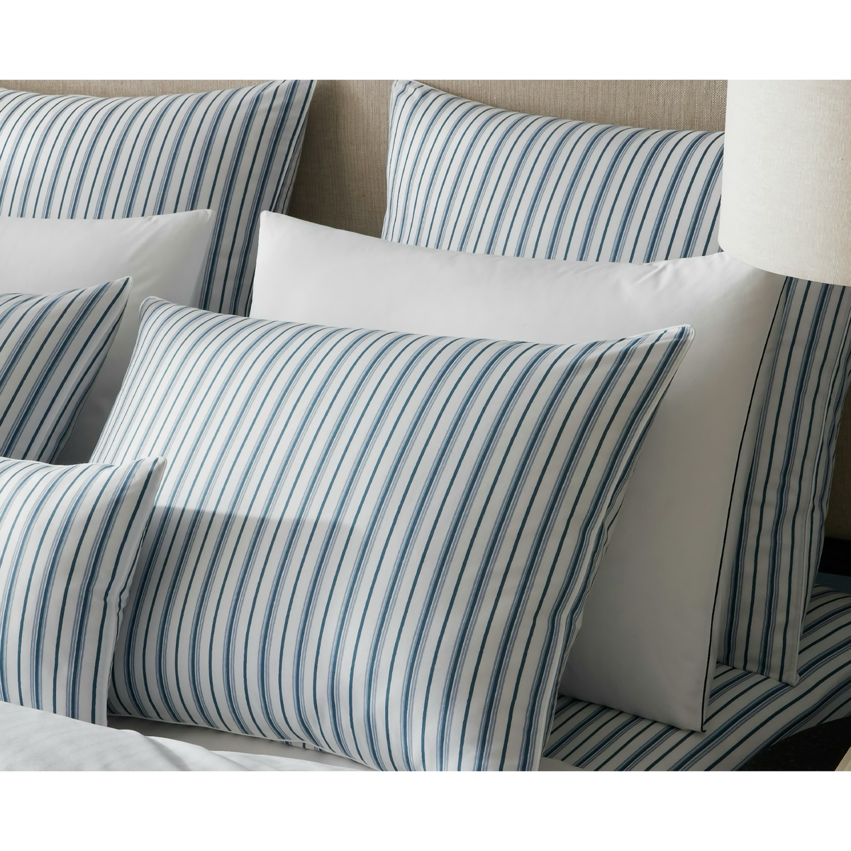 Several pillows in Prussian Blue stripes rest on Matouk Calypso Bedding