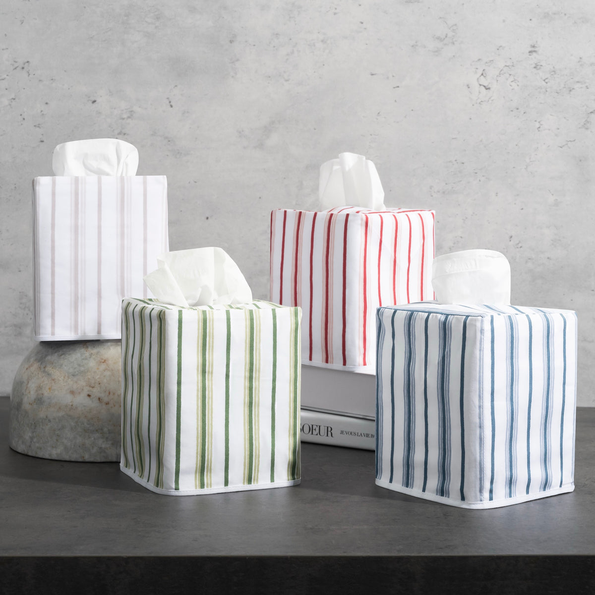 Four Matouk Schumacher Calypso Tissue Box Covers in different colors on a gray background