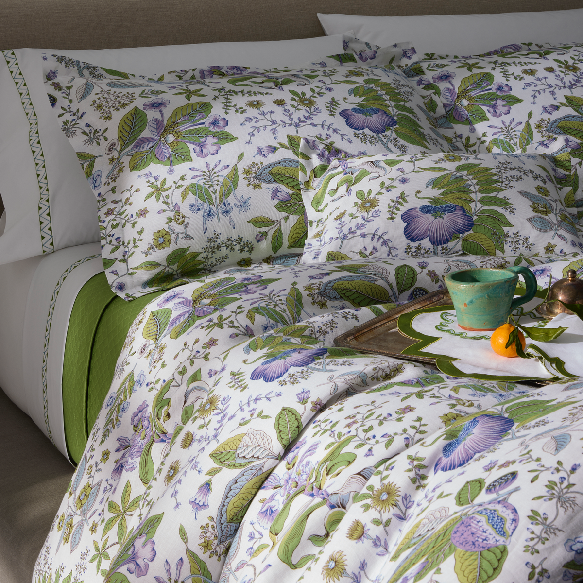 Lifestyle Picture of Side Full Bed of Matouk Schumacher Pomegranate Linen Bedding in Lilac Color with a Mug of Tea