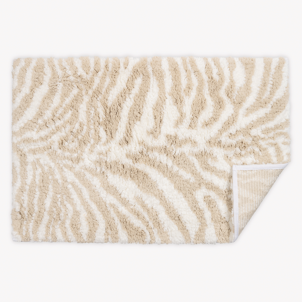 Top view of Matouk Schumacher Regine Bath Rugs in Sand color with one tip folded
