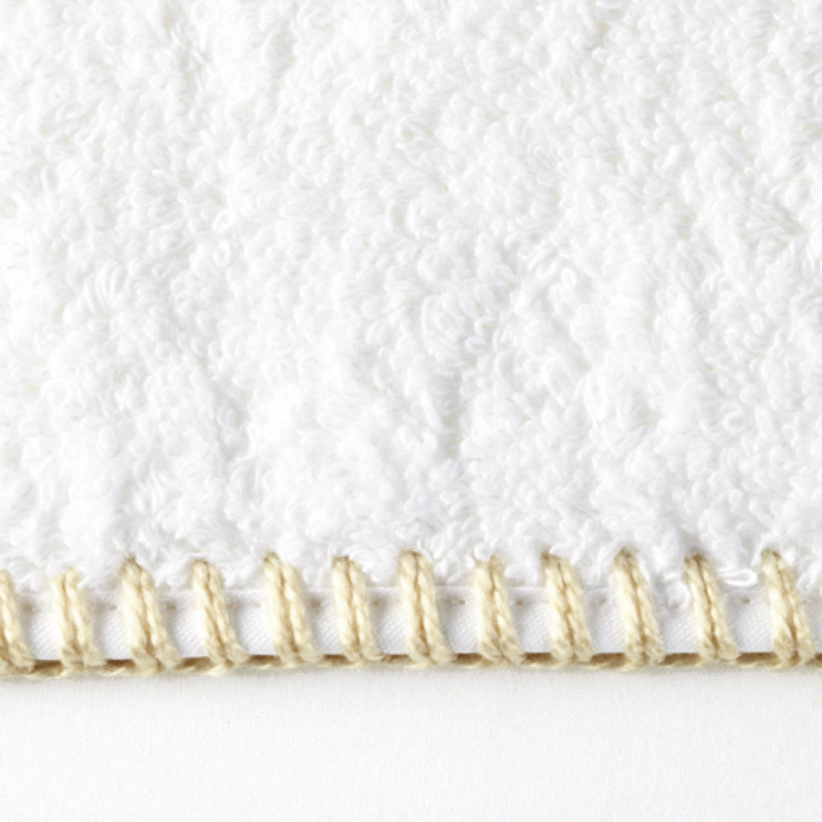 Close-up of a Matouk Whipstitch collection towel, crafted from long-staple cotton with beige stitching on white textured fabric.