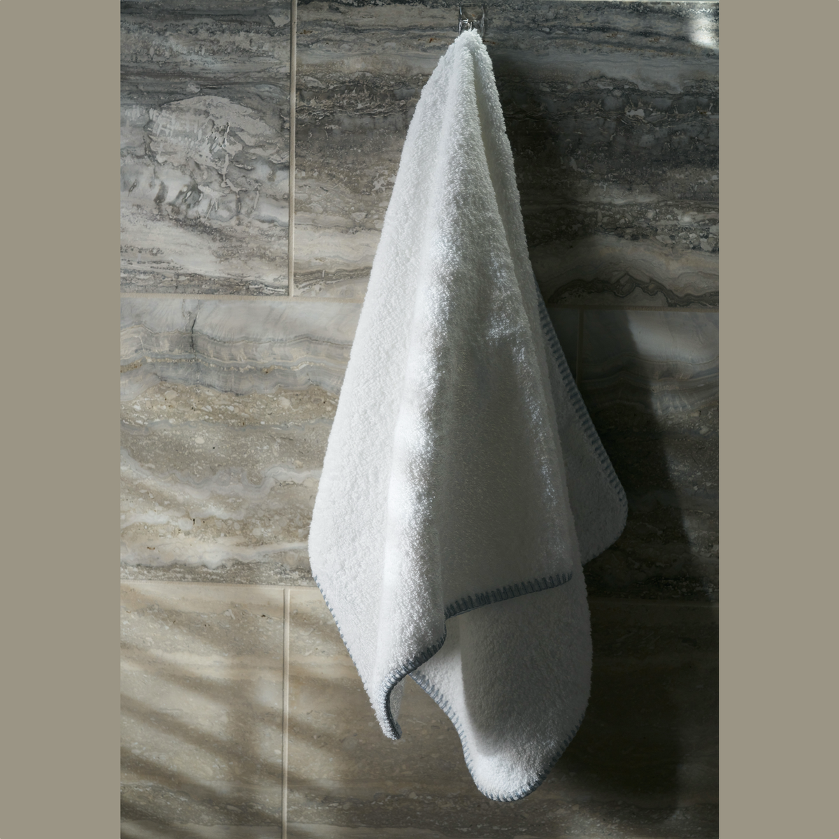 Hanging Matouk Whipstitch Bath Towel against marble wall