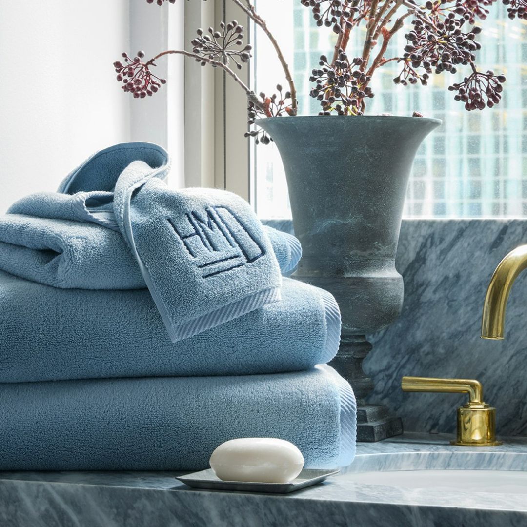 A stack of Matouk Milagro Hazy Blue towels on a sink with a bar of soap