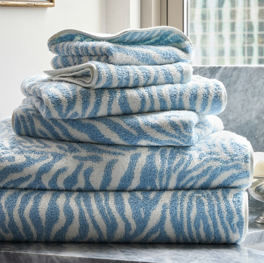 Matouk Regine Bath Towels in Hydrangea in a stack on a marble countertop