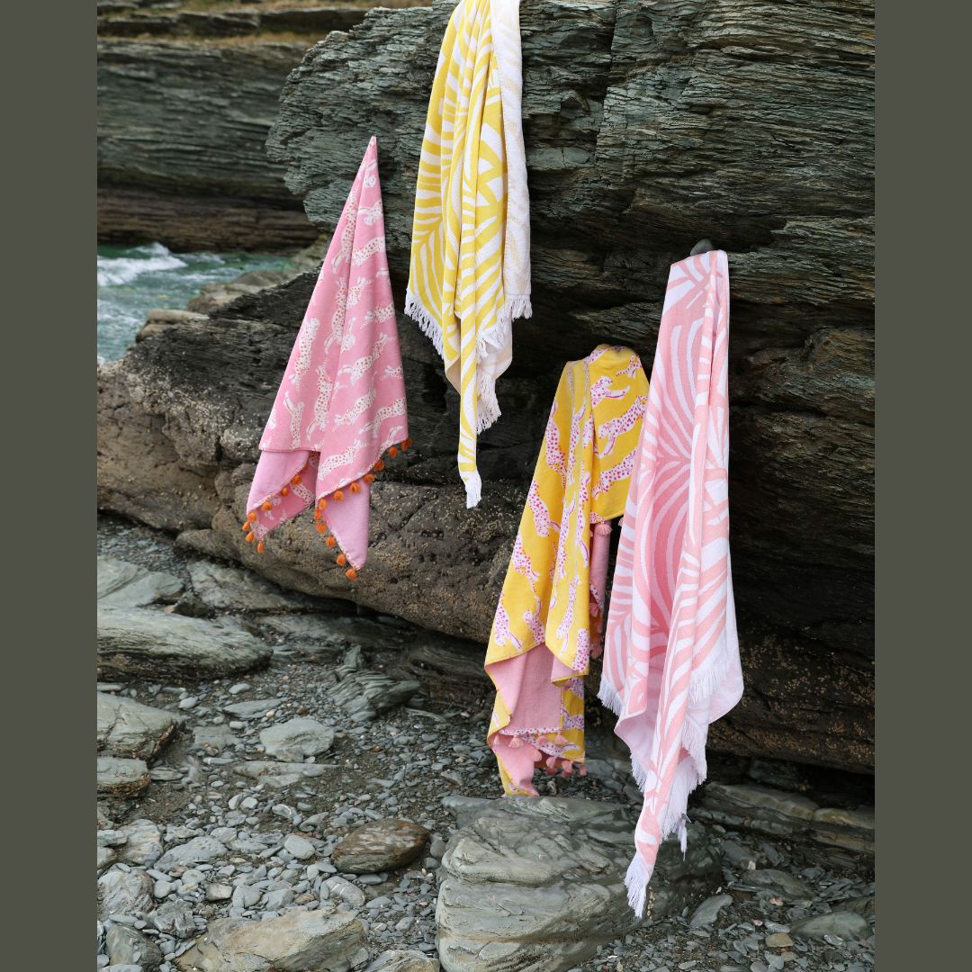 Matouk Zebra Palm and Leaping Leopard Beach Towels hanging from a cliff face by the sea