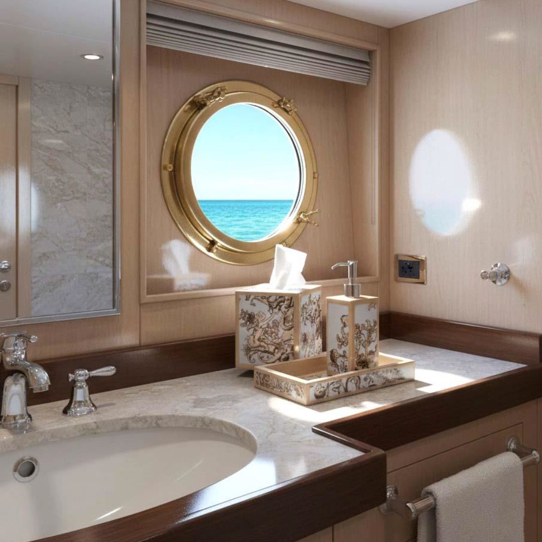 A bathroom with a marble sink, custom bath accessories, and a round porthole window showing an ocean view.
