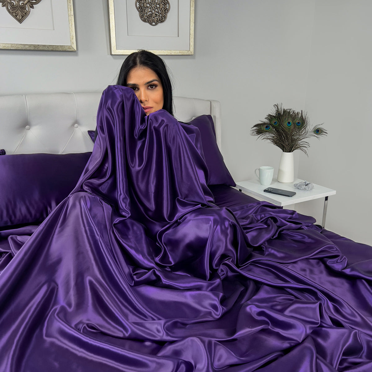 Woman sitting on a bed, wrapped in a soft plum silk sheet with a relaxed expression