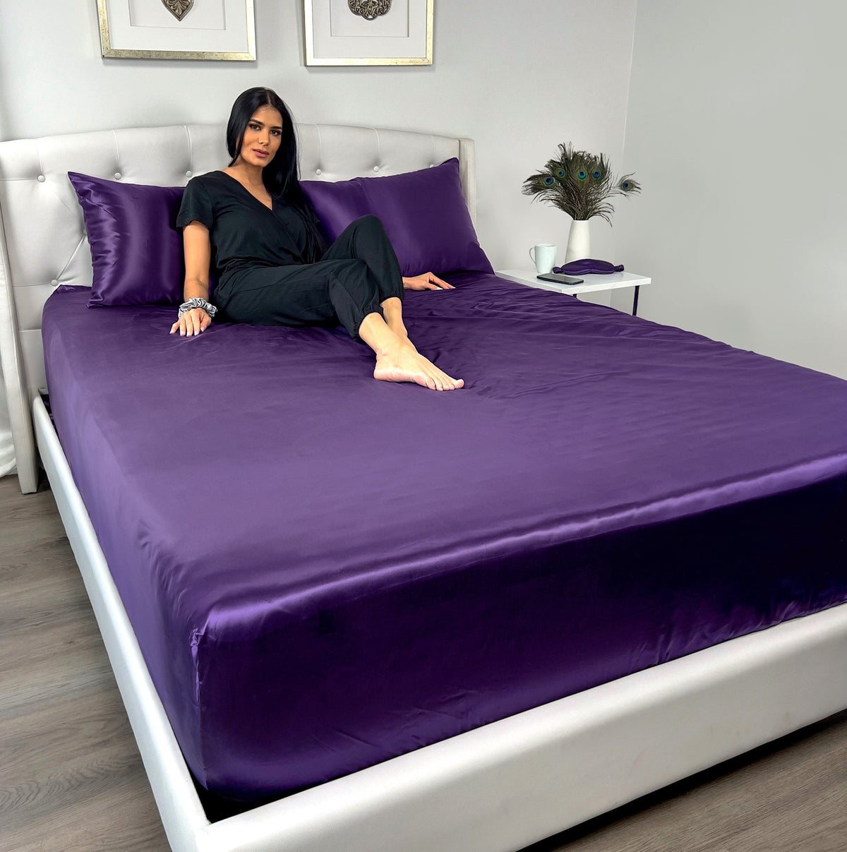Woman sitting on Plum silk fitted sheet and matching pillows on her back, wearing black outfit