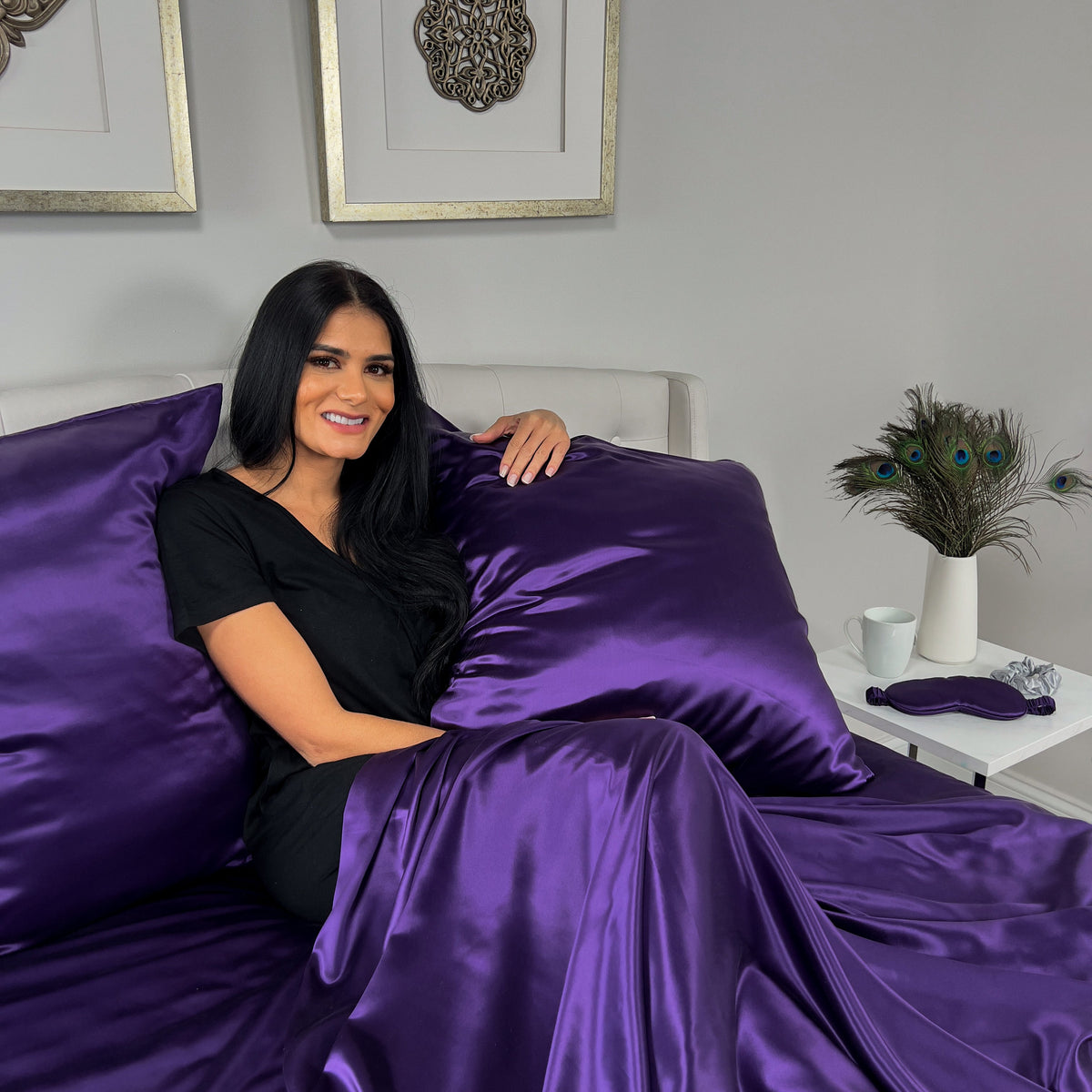 Woman sitting on bed holding with Plum silk pillow, enjoying luxurious comfort