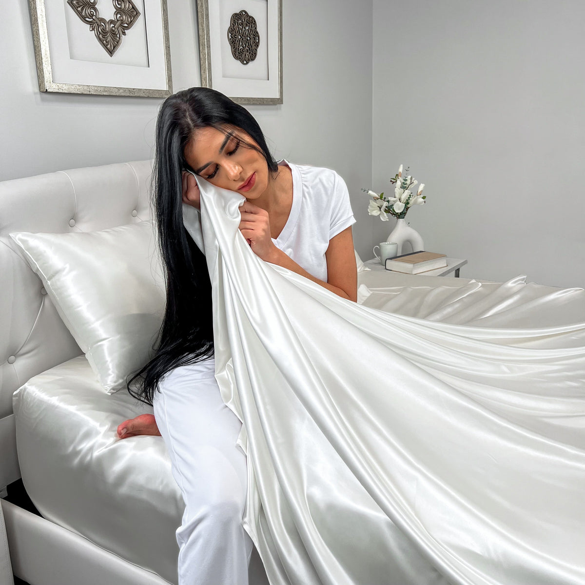 Woman sitting on a bed, wrapped in a soft ivory silk sheet with a relaxed expression