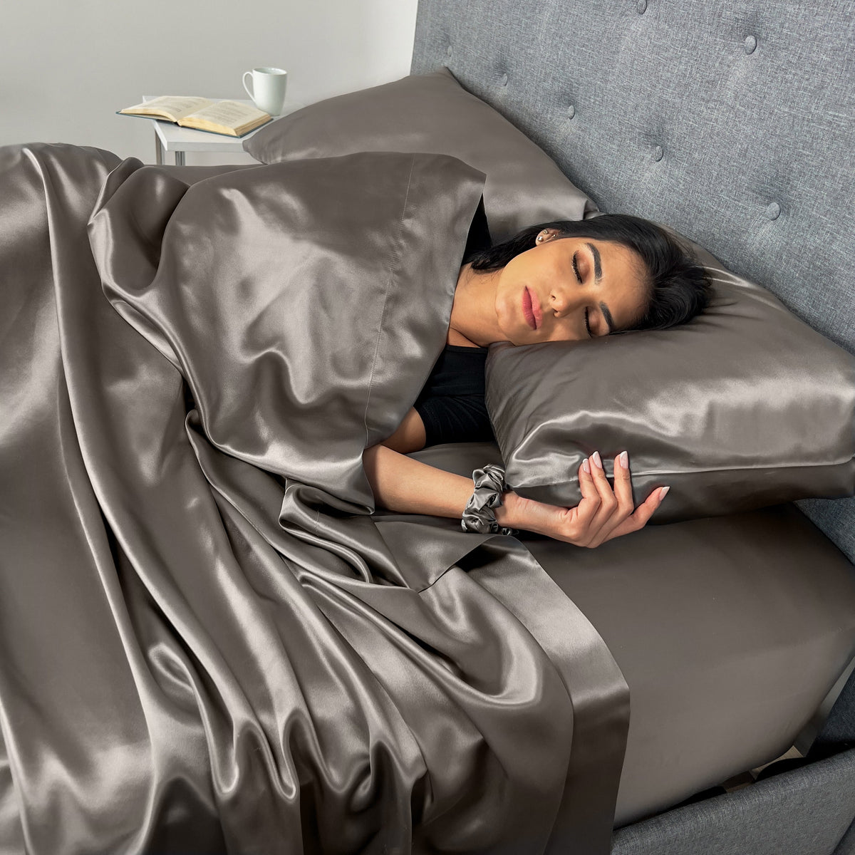 Woman wrapped in a silky gunmetal sheet, lying comfortably on a plush bed