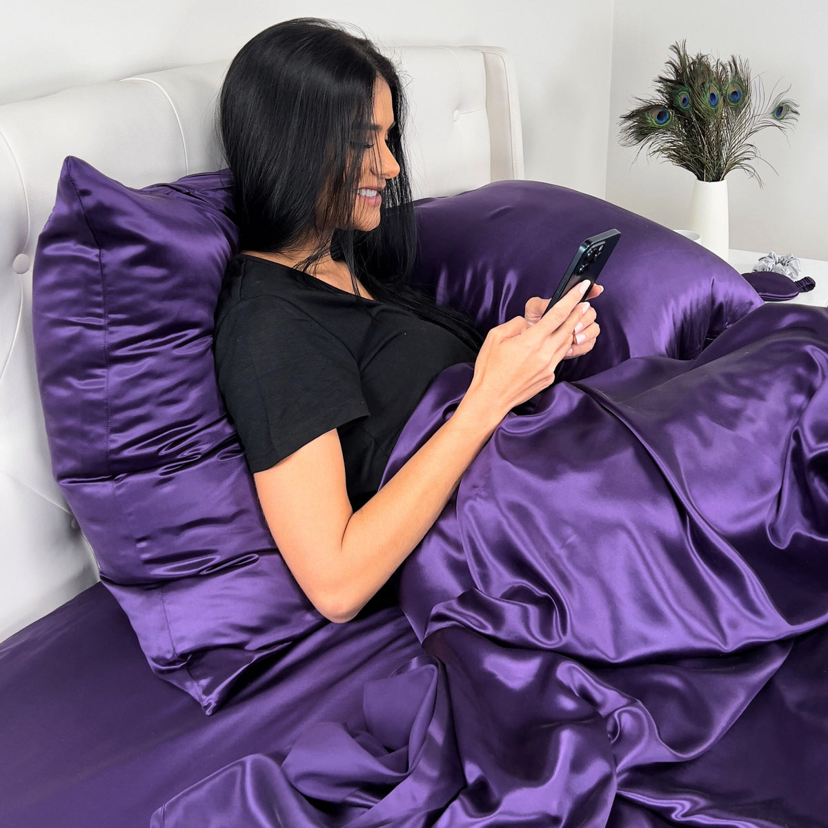 Woman lounging in bed with phone on hand and 22 Momme silk Plum luxury pillow behind her